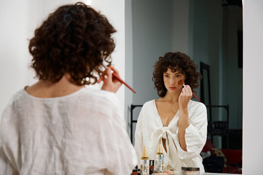 Woman Applies Makeup in a Mirror at a Bright Indoor Space