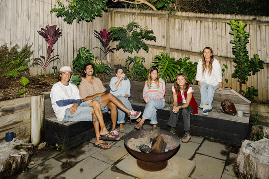 Friends relaxing by fire pit at backyard night gathering