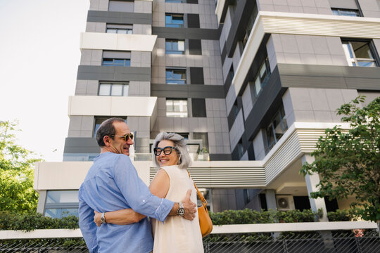 Senior couple smiling back while viewing modern apartments in summer