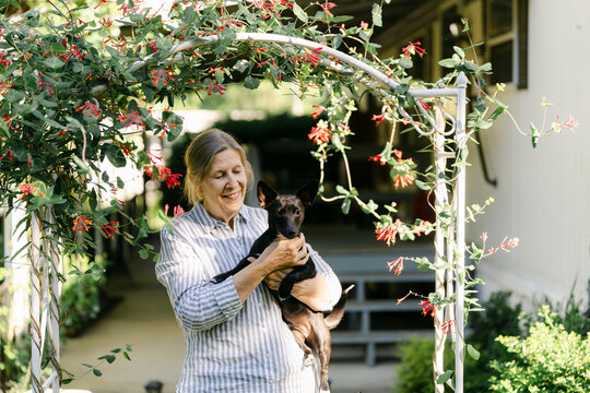portrait of woman holding her dog in front of her home