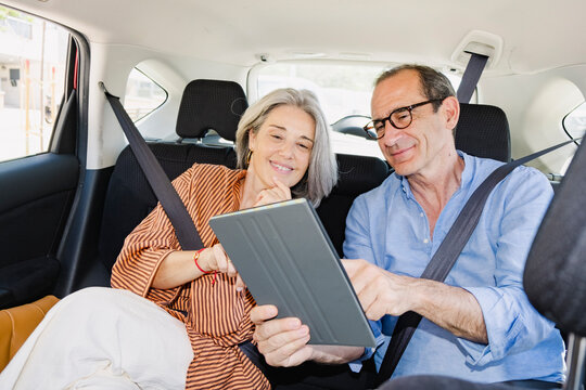 Mature senior couple using tablet together in back seat of car