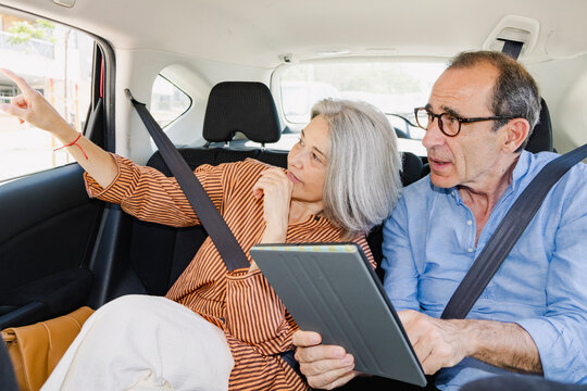 Mature senior couple checking tablet and pointing from car