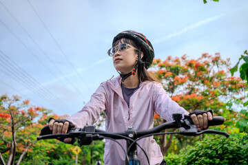 Fototapeta premium Young Asian Female Cyclist Riding Bicycle on Scenic Park Road Promoting Outdoor Fitness, Healthy Lifestyle, Cycling Adventure, Sustainable Transportation, Recreation, and Active Living