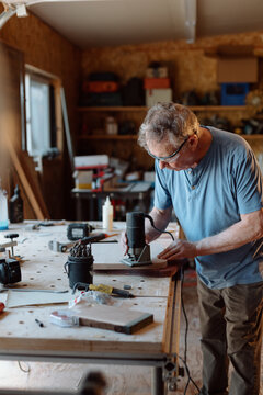 Older man woodworking in a workshop using a hand router