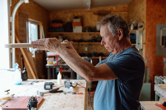 Older man inspecting wooden part in a home woodworking workshop