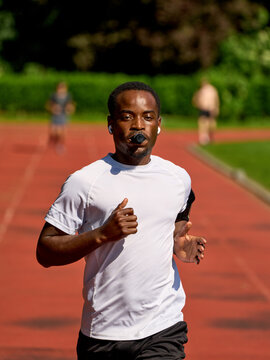 Man Runs on a Track in a Park While Wearing Earbuds
