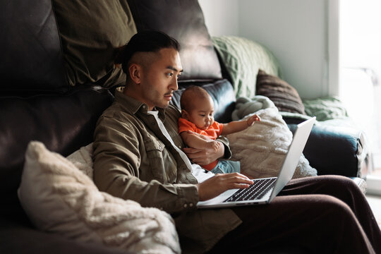 Asian father multitasking working with baby on laptop
