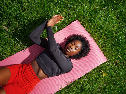 Young Black Woman Stretching on Pink Yoga Mat in Sunny Meadow