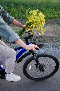 Person riding bicycle with yellow wildflowers on handlebar