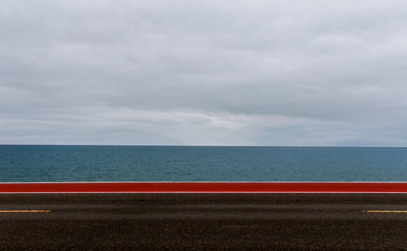 Minimalist landscape: Grey sky, blue lake, and red-and-black highway.