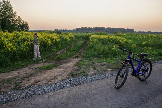 Woman standing beside bike at sunset in flowering field
