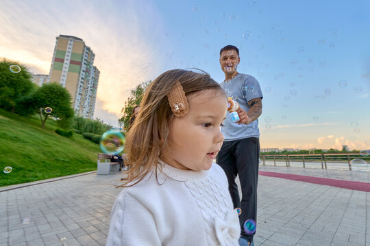 Toddler Chasing Soap Bubbles with Father Playing Outdoors