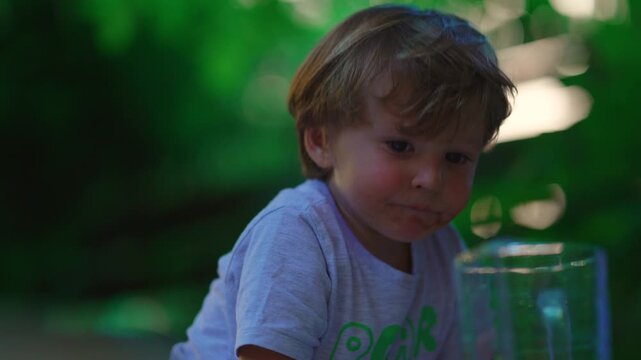 Curious toddler eating snack outdoors in family garden, quietly observing surroundings, expressing wonder, healthy childhood, outdoor exploration, independence