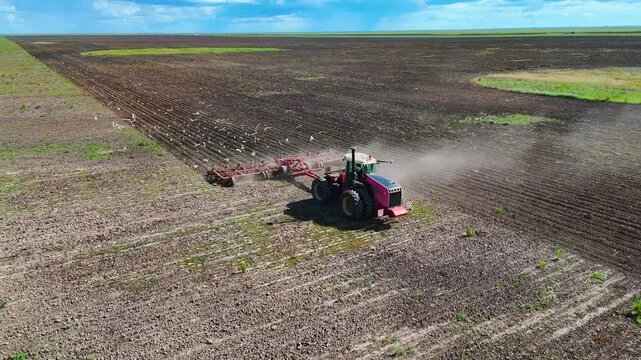 Tractor cultivating the soil in a field before planting, drone view.