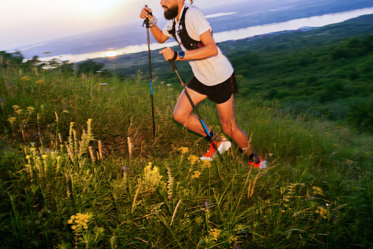 Man Runs on a Hill at Sunset With Hiking Poles and Green Grass