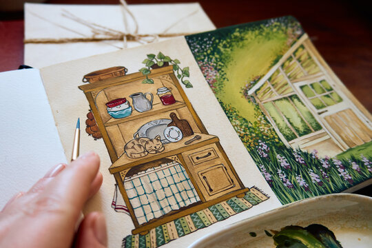 Artist painting a cozy cottagecore illustration in a sketchbook