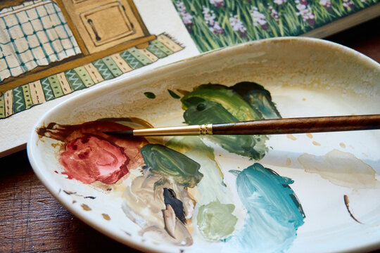 Paintbrush resting on a ceramic watercolor palette with mixed paints