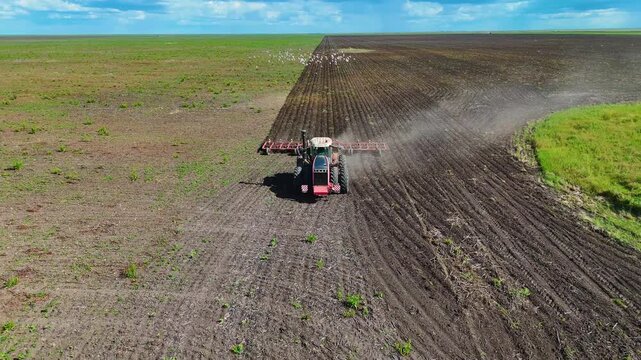 Tractor cultivating the soil in a field before planting, drone view.