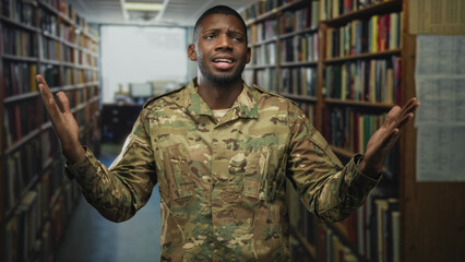 Soldier man in camouflage with pained face holding his upper arm and raised hands amid tall bookshelves in a library building  frustration. © Krakenimages.com