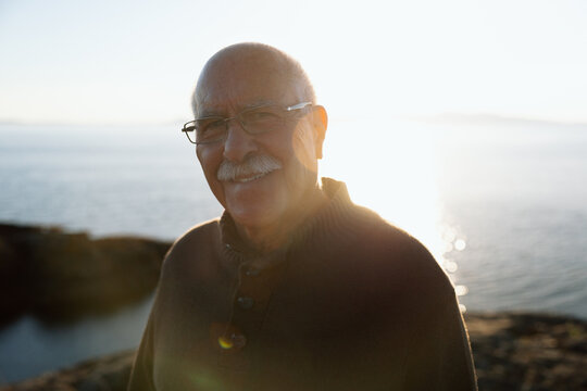 Candid portrait of a smiling senior man by the ocean at sunset