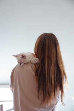 Woman with long hair holding a kitten on her shoulder