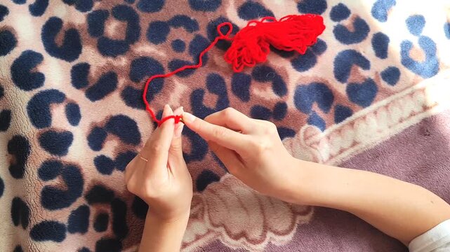  Person holding red yarn for knitting and crochet craft, hands working with fiber thread, handmade hobby.