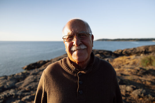 Senior man smiling on rocky coast at golden hour