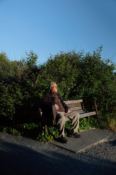 Elderly man sitting on park bench in golden sunlight, thoughtful