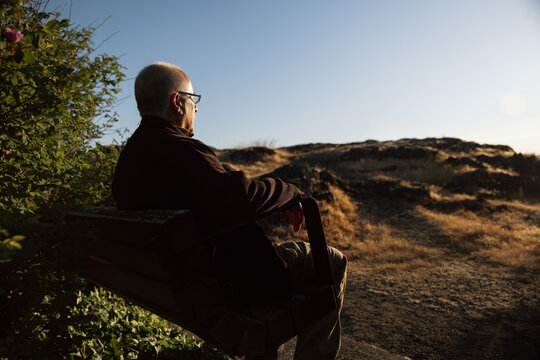 Elderly man sitting on bench watching sunset in quiet landscape