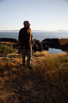 Elderly man on rocky coast at sunset in peaceful contemplation