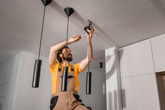 Man installing pendant lights on ceiling in modern kitchen while using screwdriver