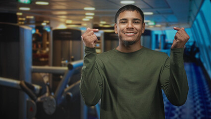 Fototapeta premium Man smiling and showing hands and face while making finger heart gesture at airport gate with terminal windows and seating; joy.