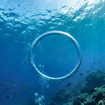 A perfect bubble ring floating underwater in the clear blue ocean above a coral reef