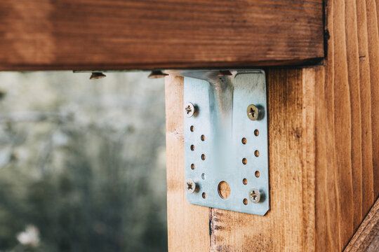 Galvanized metal joist hanger bracket secured with screws on wooden beam. Construction concept.