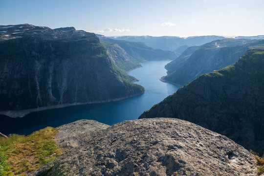 High-angle drone-style landscape of a deep fjord between steep mountain cliffs under clear summer sky in Norway.