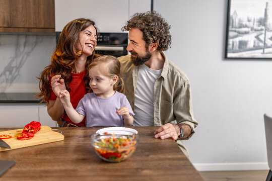 Caucasian family cooking together in modern kitchen with smiling parents and little daughter