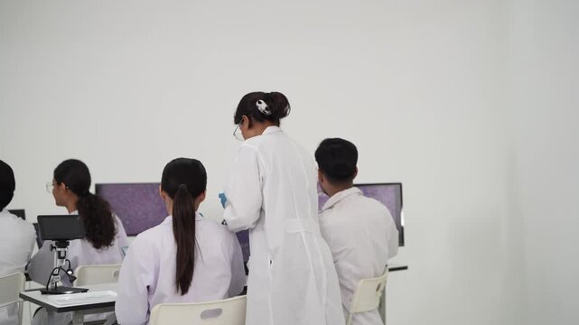 Scientist looks into a microscope while teammates observe magnified tissue on a monitor during a hands on laboratory training session in a pathology research lab