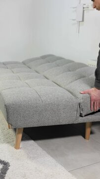 Vertical footage of demonstrating a versatile grey sofa bed, transforming it into three different positions: fully flat for sleeping, semi-reclined for lounging, and upright for sitting.
