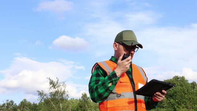 Ecologist is talking on walkie-talkie radio. Meteorologist or climatologist holds a tablet and monitors the impact of global warming and climate change