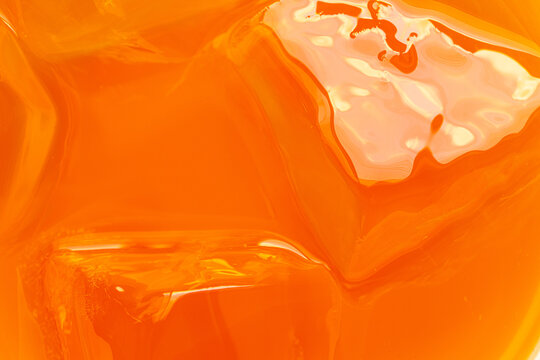 Macro abstract background of bright orange juice or fruit beverage with ice cubes texture,Close-up macro shot of vibrant bright orange juice or fruit drink surface with ice cubes, highlighting liquid 