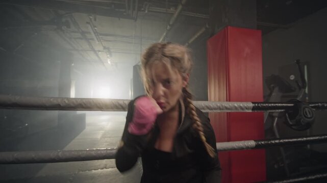 Portrait of young Caucasian woman shadowboxing inside boxing ring, throwing punches towards camera. Clip suitable for fitness brand marketing and motivational sports campaigns