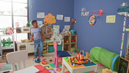 African american boy reaching for wall dartboard while holding toy car in colorful classroom  playful curiosity. © Krakenimages.com