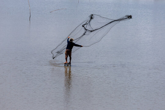 Fisherman standing on a stool in open water throwing a black fishing net.