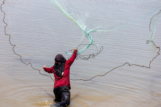 Fisherman throwing a cast net into shallow water during a bright sunny day.
