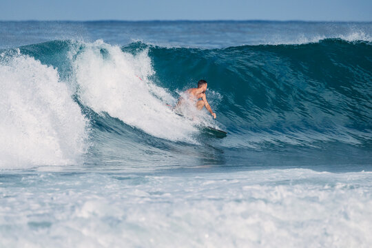 Surfer riding a powerful blue ocean wave on a sunny day in Bali