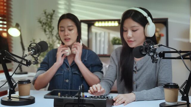 Podcaster content influencer creator podcast studio microphone headphone set in bright home studio, two young women record and mix audio with focus, creating engaging talk for social media