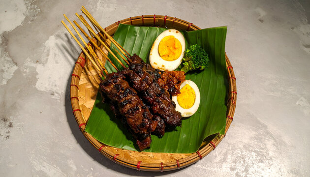Delicious Satay Skewers with Hard-Boiled Eggs and Greens on Banana Leaf.