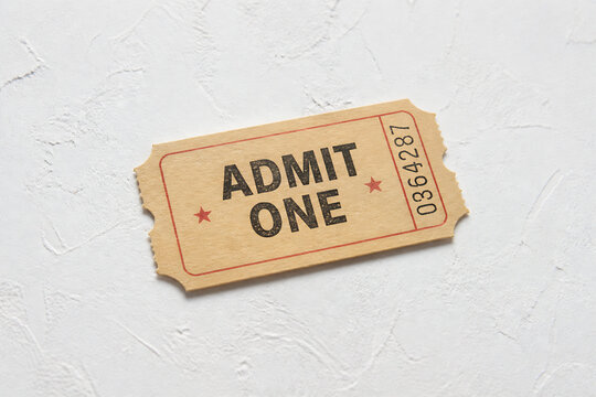 A worn, rectangular admission ticket with the words ADMIT ONE and a serial number on a white textured surface.