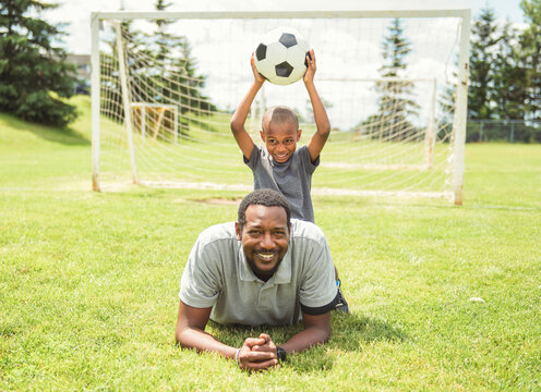 father with son playing football or soccer outside on field