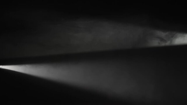 A white spotlight crosses dense smoke on a black background. Concept of overlay real effect, theater, concert, cinema, event, advertising, presentation, backdrop, and dramatic design.
